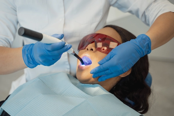 Dentista aplicando luz de curado durante un tratamiento dental en una paciente